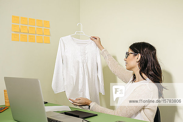 Young woman sitting at desk in office examining garment