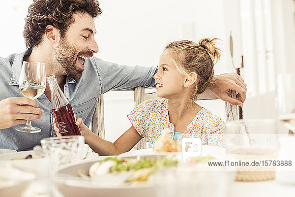 Father and daughter sitting at dining table toasting