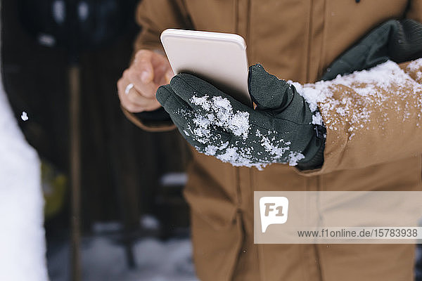 Männerhand hält Smartphone im Winter  Nahaufnahme