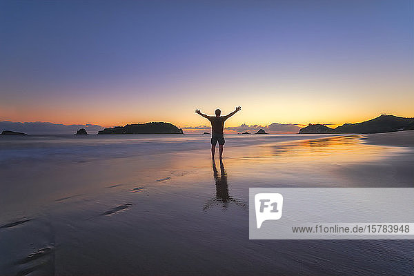 Mann hebt bei Sonnenuntergang die Arme am Strand von Hahei Beach  Waikato  Nordinsel  Neuseeland