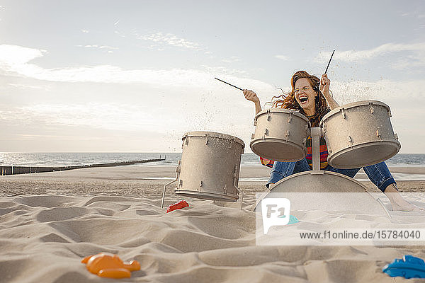 Porträt einer lachenden Frau beim Trommeln am Strand