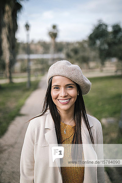 Porträt einer lächelnden jungen Frau mit Baskenmütze in einem Park