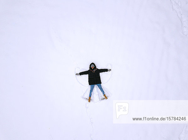 Frau liegt auf Schnee und macht Schnee-Engel