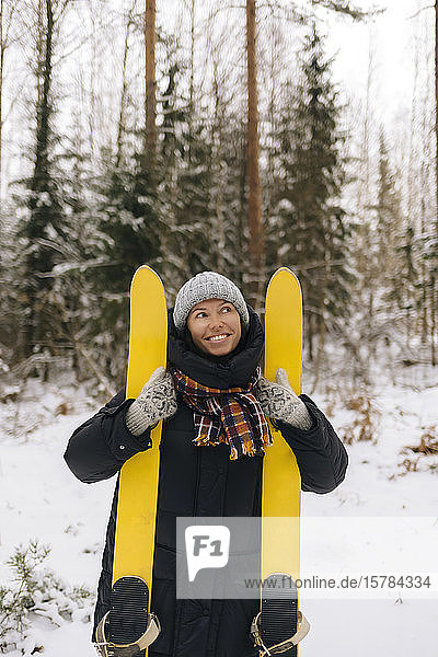 Portrait of smiling woman with skis in winter forest