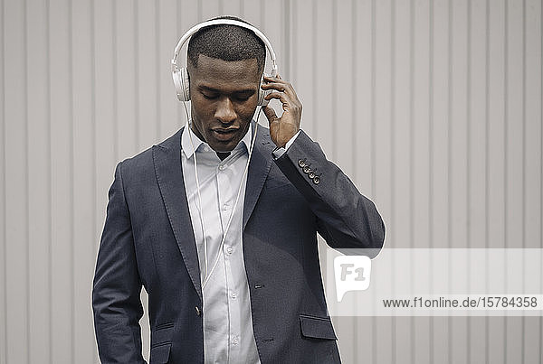 Portrait of young businessman with eyes closed listening music with headphones outdoors