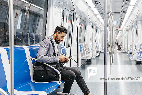 Young businessman with cell phone and earphones on the subway