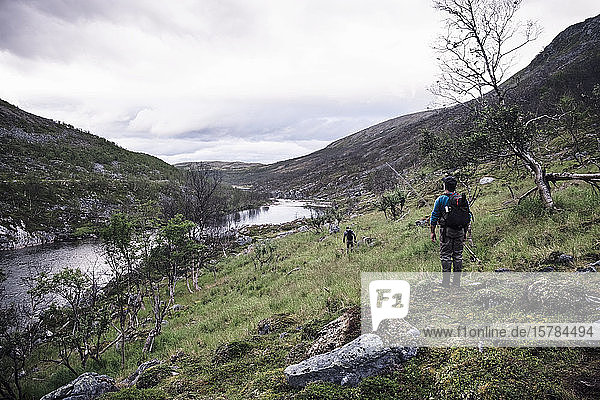 Fly fishermen hiking along river bank with mountains  Lakselv  Norway