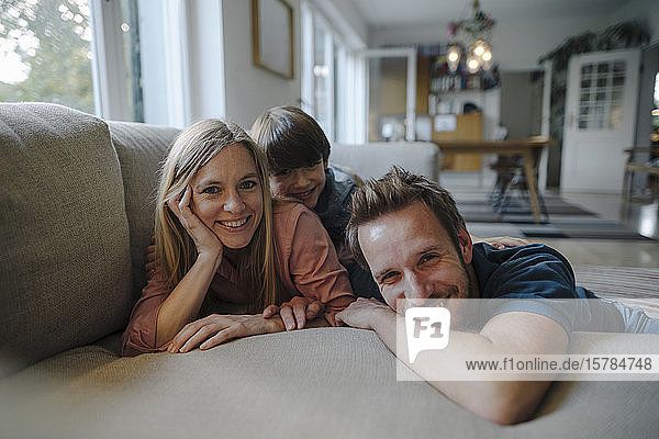 Glückliche Familie liegt auf der Couch und lächelt in die Kamera