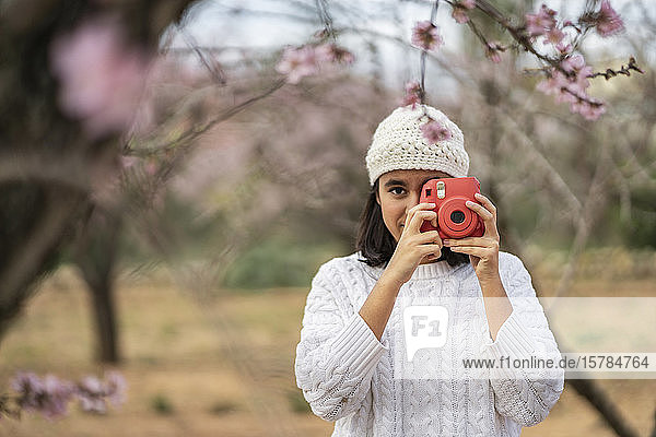 Porträt einer Teenagerin  die mit der Kamera zwischen blühenden Mandelbäumen fotografiert