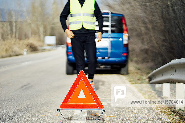 Man putting warning triangle on country road by van breakdown