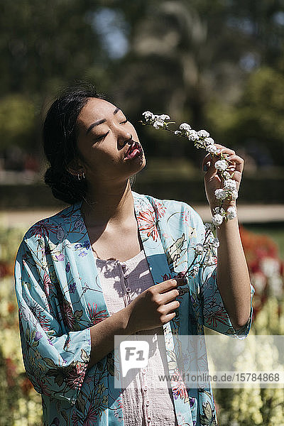 Schöne junge Frau hält im Frühling eine Blume in einem öffentlichen Garten