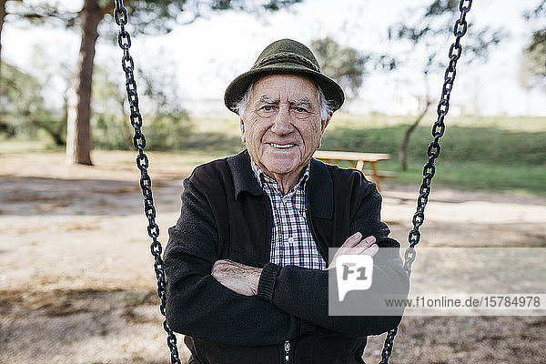 Old man sitting on swing in park with arms crossed