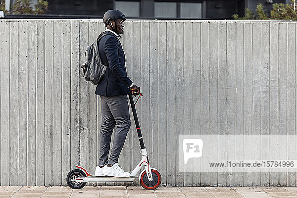 Smiling businessman on push scooter in front of concrete wall