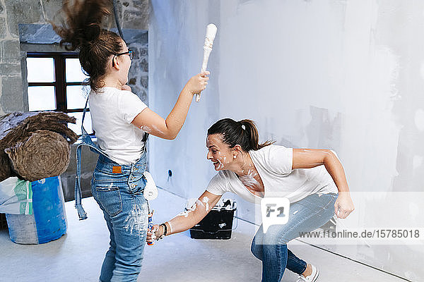 Playful mother and daughter having fun while painting a wall of her new house