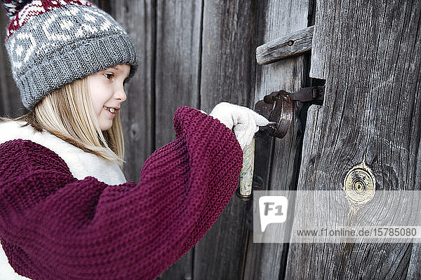 Lächelndes Mädchen mit Wollmütze entriegelt Holztür