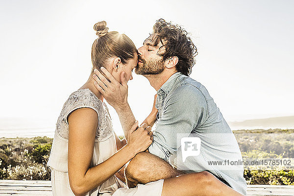 Zärtliches junges Paar auf Terrasse an der Küste im Sommer