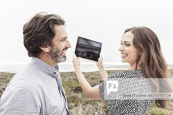 Glücklicher Mann sieht seine Frau mit Tablette in der Hand an der Küste