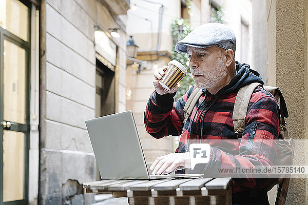 Porträt eines älteren Mannes mit Kaffee zum Mitnehmen  der mit seinem Laptop im Straßencafé sitzt  Barcelona  Spanien