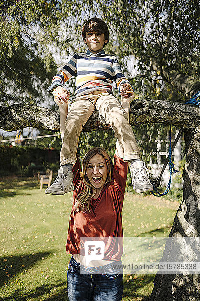 Boy climbing tree  sitting on branch  mother holding his hands