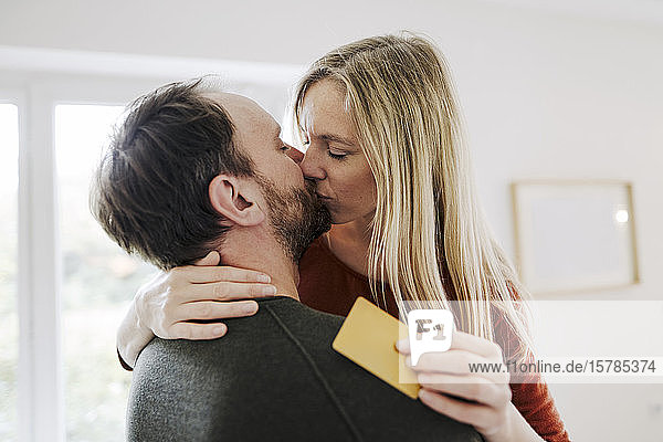 Glückliches Paar steht zu Hause  küsst sich  hält eine Kreditkarte