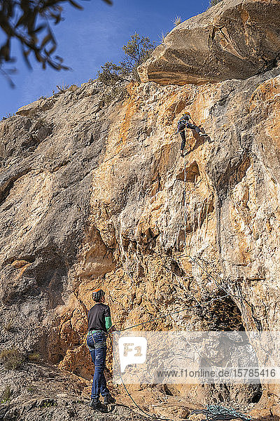 Man securing woman climbing at rock face