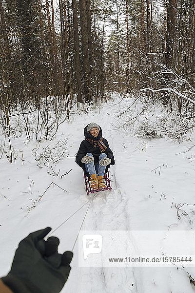 Man's hand pulling woman sitting on a sledge