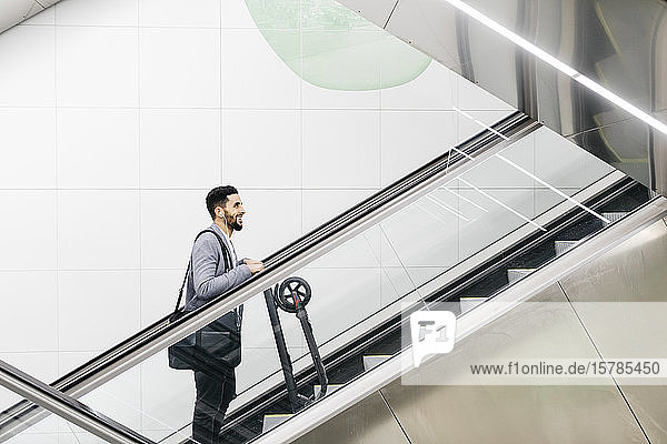 Smiling young businessman with electric scooter on escalator