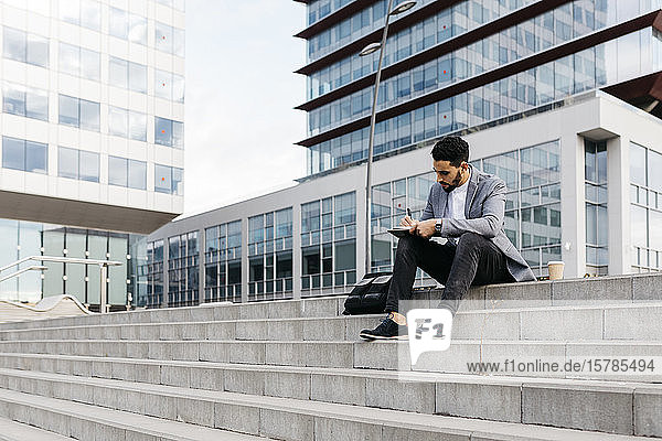 Casual young businessman sitting on stairs in the city taking notes