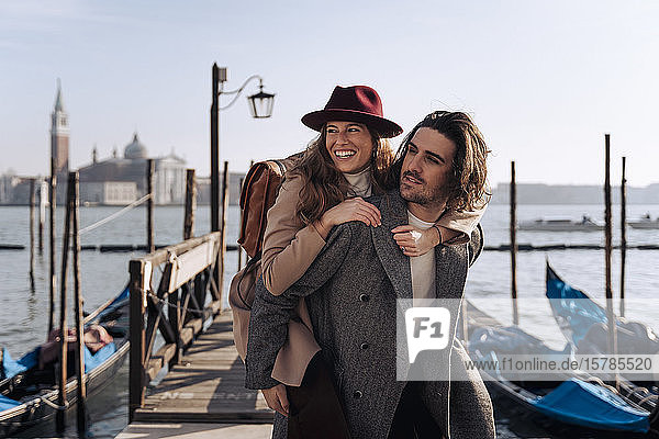 Young man giving his girlfriend a piggyback ride at the waterfront in Venice  Italy