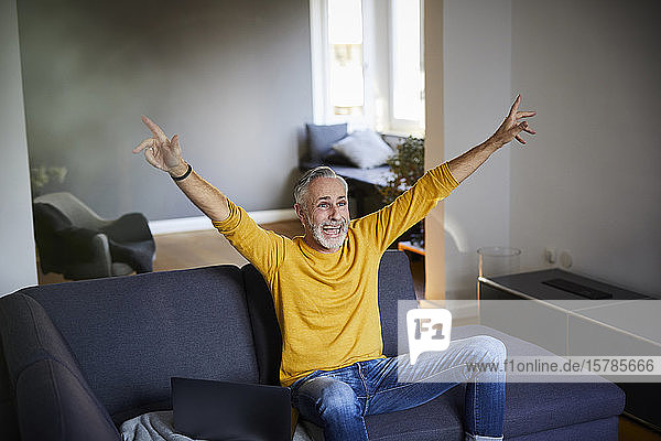Mature man sitting on couch at home cheering
