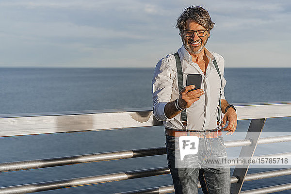 Lächelnder Mann mit Smartphone auf einem Steg