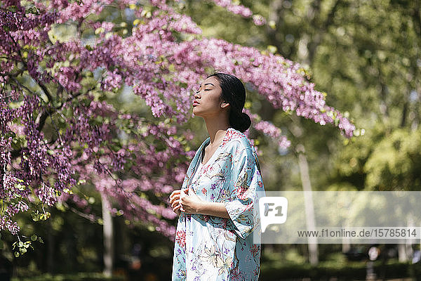 Hübsche junge Frau mit blühendem Kirschbaum in einem öffentlichen Garten im Frühling