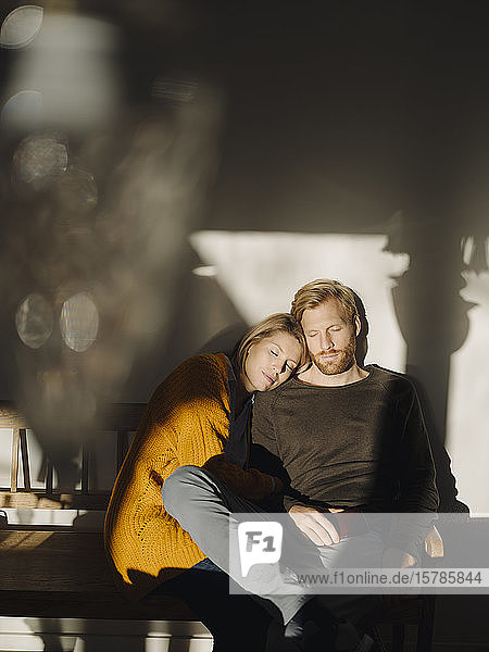 Entspanntes Paar  das zu Hause im Sonnenlicht auf einer Bank sitzt