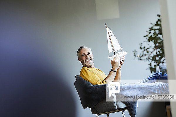 Smiling mature man at home holding model sailboat