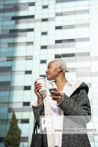 Stilvolle Geschäftsfrau  die mit Kaffee und Smartphone durch die Stadt pendelt