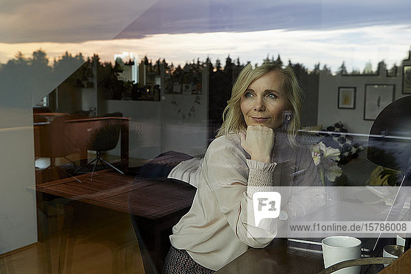 Portrait of blond woman with laptop behind windowpane at home