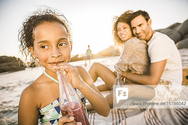 Mädchen mit ihrer Familie bei Sonnenuntergang am Strand bei einem Erfrischungsgetränk