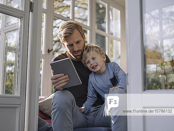 Father and son using tablet in sunroom at home