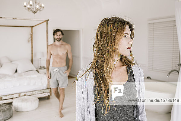 Porträt einer seriösen jungen Frau im Schlafzimmer mit Mann im Hintergrund