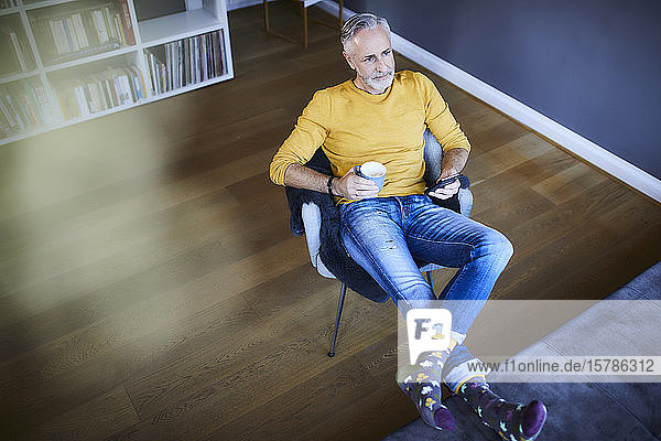 Relaxed mature man at home with cell phone and cup of coffee