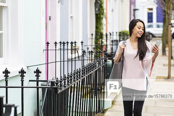 Porträt einer lächelnden Frau auf dem Bürgersteig  die auf ihr Handy schaut  Notting Hill  London  UK