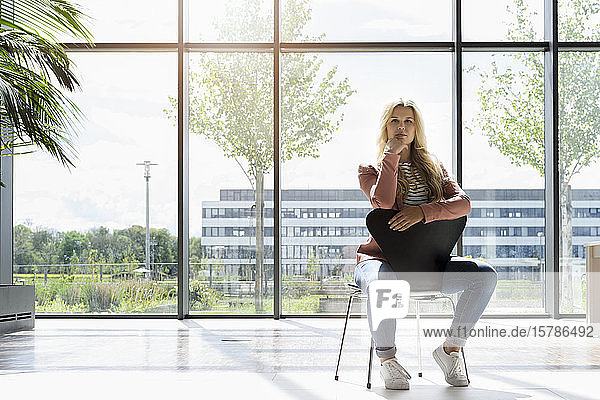 Blonde Geschäftsfrau auf Stuhl sitzend  im Hintergrund das Bürogebäude