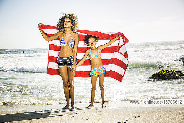 Glückliche Mutter und Tochter mit Handtuch am Strand stehend
