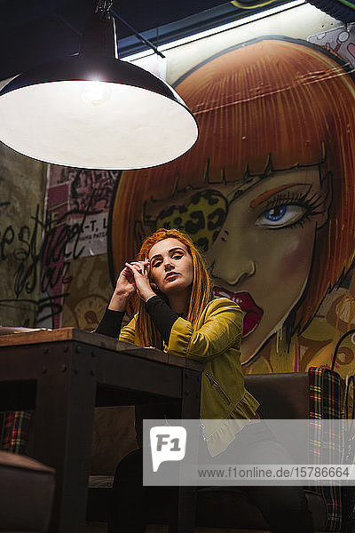 Porträt einer rothaarigen jungen Frau  die in einer Kneipe vor einer Graffiti-Wand wartet