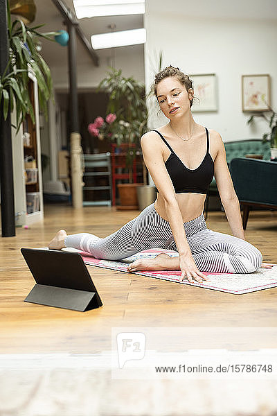 Young woman practicing yoga at home  using yoga app on digital tablet