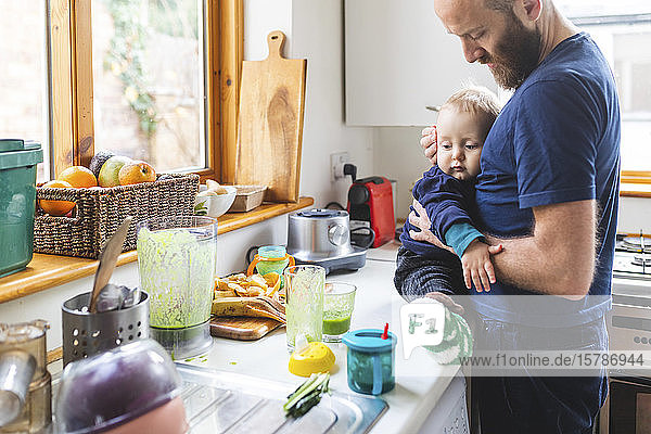 Mann in der Küche  der Essen zubereitet und mit seinem Sohn kuschelt