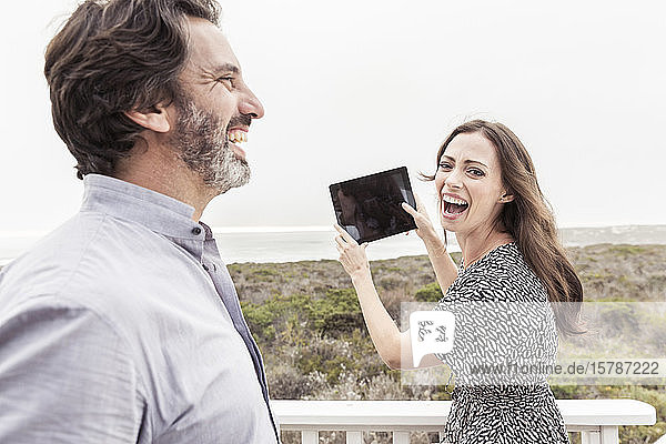 Glücklicher Mann mit Frau hält Tablette an der Küste