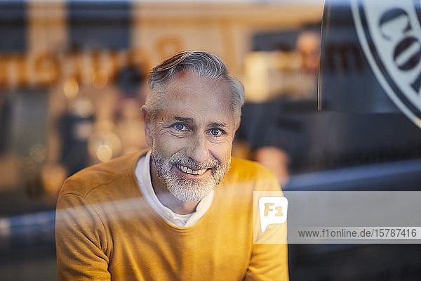 Portrait of smiling mature man behind glass pane in a cafe