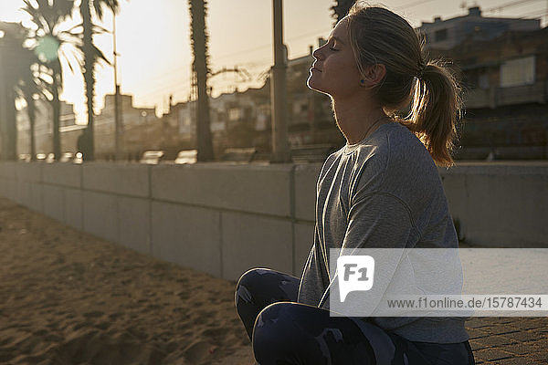 Sportliche junge Frau macht bei Sonnenuntergang eine Pause auf der Strandpromenade