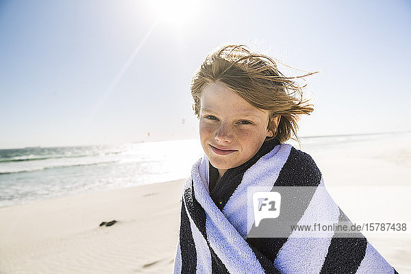 Porträt eines lächelnden  in ein Handtuch gewickelten Jungen am Strand